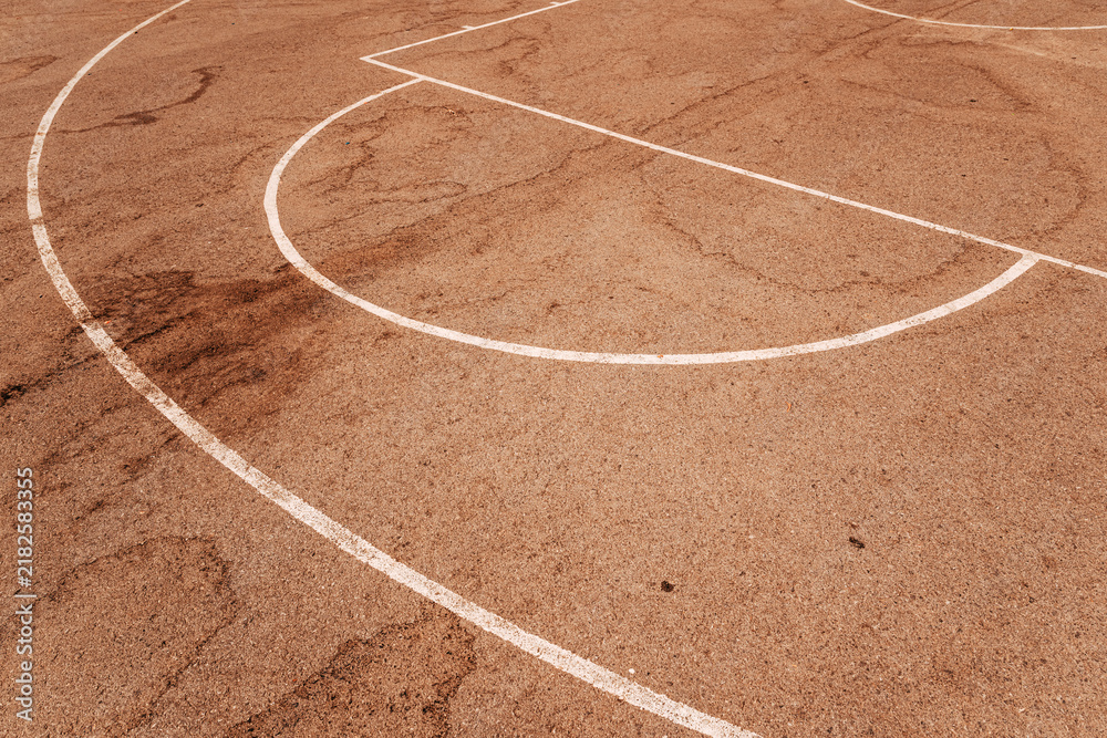 Obraz premium High angle view of white painted game lines on a reddish-brown asphalt outdoor basketball court surface.