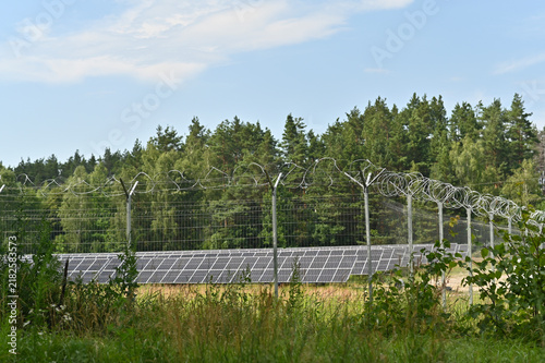 Canvas Print Row of solar panels enclosed behind secure wire fence near forest outdoors