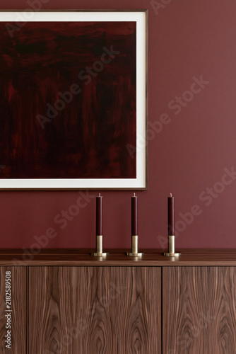 A burgundy interior features a large abstract painting above a wooden cabinet with three slim candles in brass holders.
