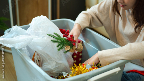 Young woman in cozy sweater organizing holiday decorations and festive ornaments into Storage Bin After the Holidays