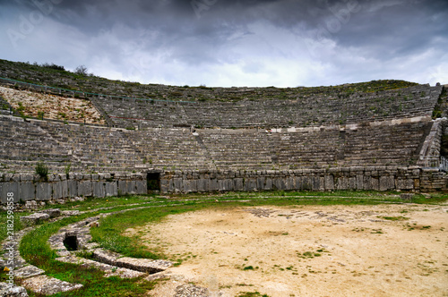 Bild auf Leinwand Curved stone seating tiers of the Ancient Theatre of Dodona under dramatic storm