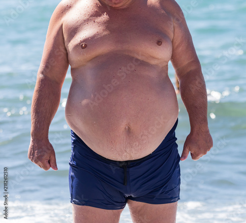 Quadro su tela Overweight man stands near ocean waves