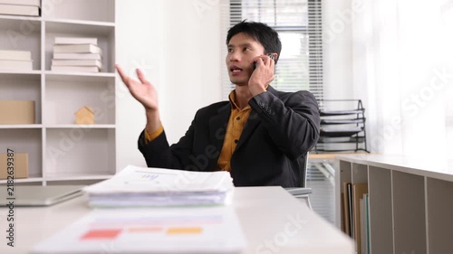 Asian businessman talking on a smartphone, negotiating a business deal. Corporate manager discussing sales in office.