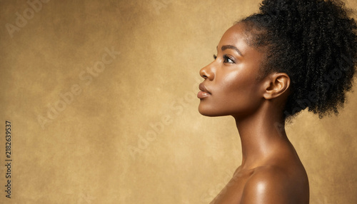 Profile portrait of attractive dark skin Black woman with curly hair updo on warm gold background natural beauty concept