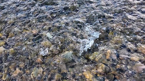 The flow of a clear, clean mountain river in the shallows, natural background, slow motion