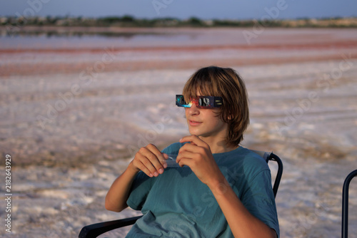 Konstfotografi Young boy wearing solar eclipse glasses, looking forward while sitting outdoors