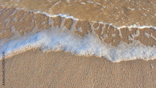 Bild auf Leinwand Ocean waves gently wash over sandy beach, creating foam patterns and ripples as