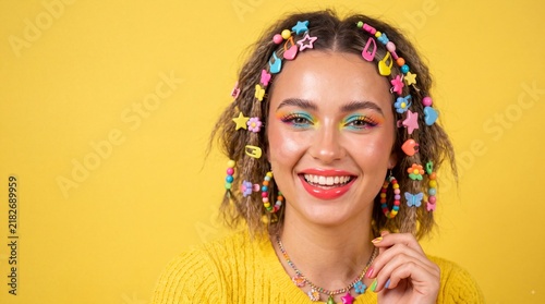 Happy young woman wearing colorful hair accessories and makeup smiling at camera against yellow background
