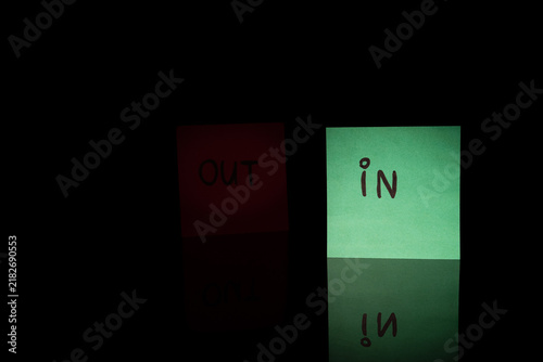 Fotografía Illuminated green IN sticky note next to dark shadowed OUT note on black background with reflection
