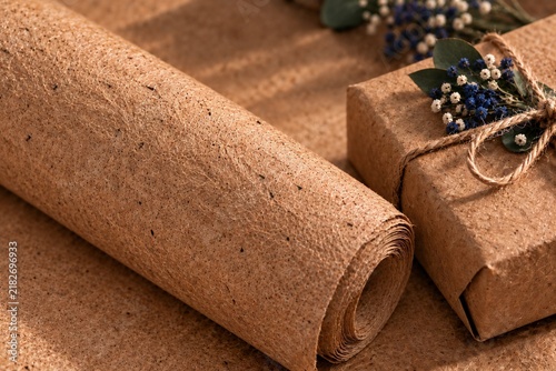 A brown roll of coarse kraft paper with a wrapped gift and floral decor.