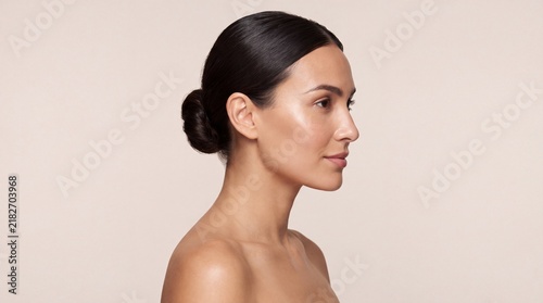 Side profile portrait of a beautiful woman with smooth skin and hair in a bun with neutral background with against plain neutral