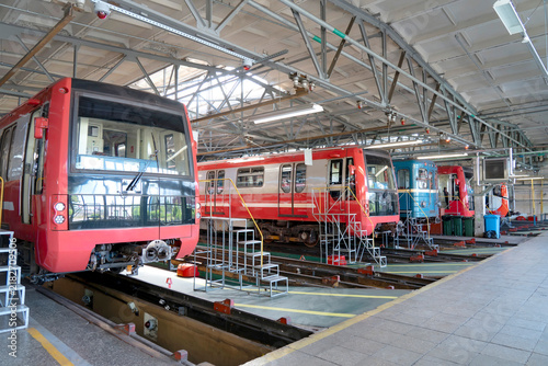 Subway trains sit in a maintenance depot for repairs and inspections during the bright daytime in a large indoor industrial facility