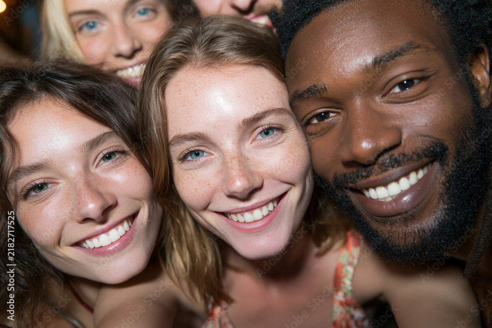 Fototapeta premium Bright smiles fill the frame of three close friends. Warm lighting enhances joyful, genuine expressions. They lean in for a fun, intimate selfie moment