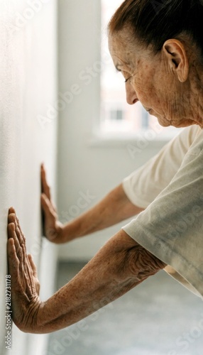 Senior functional fitness concept. Elderly person stretching arms against a wall in a bright room, focusing on health and mobility.