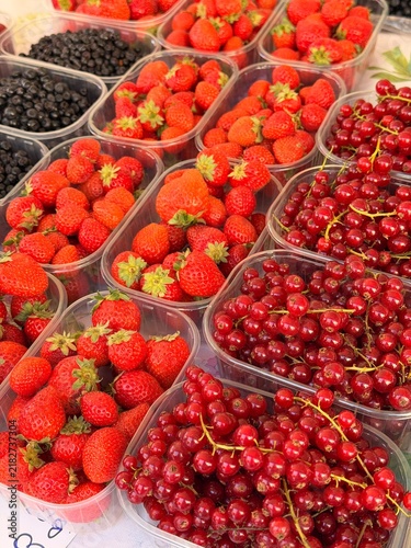 Assorted fresh berries in plastic containers at farmers market - raspberries, blackcurrants and blueberries for sale