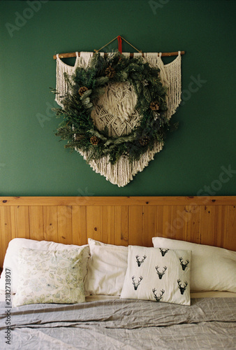 A bed with a wooden headboard beneath a macrame and evergreen wreath.