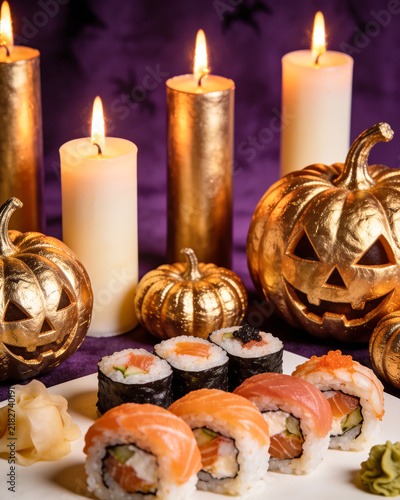 Sushi Halloween on dark background. Philadelphia maki roll, carved pumpkins, candles. Creative party food. Spooky, purple, golden, scary, fun, bewitched. Japanese sushi bar, restaurant holiday menu