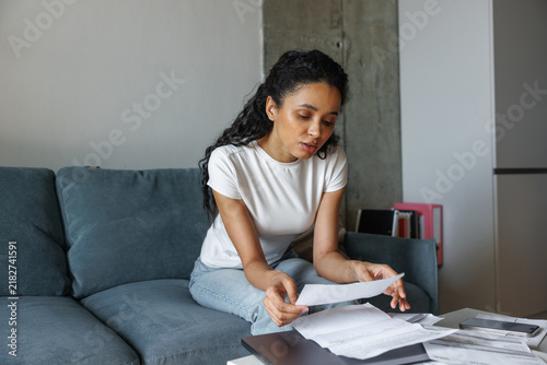 Concentrated black dark-haired woman checking financial documents