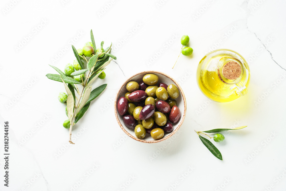 Obraz premium Olives in wooden bowl and fresh olive tree branch at white background.