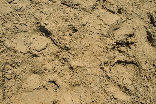 An abstract texture of yellow-brown construction aggregate sand with a shoe sole indentation
