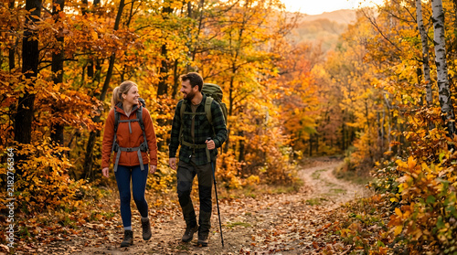 A couple hiking on a path through a vibrant autumn forest, surrounded by trees with golden and orange leaves