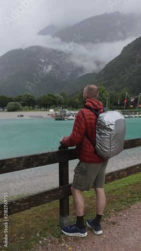 Man stands by a railing and admires a beautiful mountain lake beneath dramatic clouds after the rain.