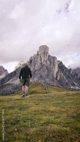 Solo hiker walking through a scenic mountain trail in the Italian Dolomites, exploring wild alpine nature with dramatic rocky peaks and beautiful summer landscape.