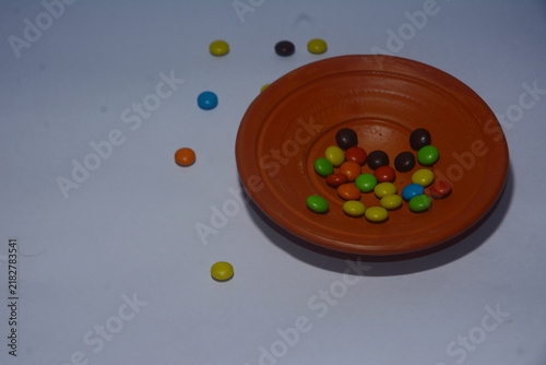 Obraz na płótnie Colorful chocolate candies inside an earthen bowl on a neutral table