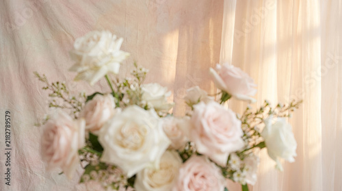 Romantic soft pink and white rose bouquet against warm pastel fabric background drapery.