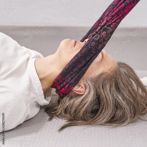 Cuadro en lienzo Mature Woman Performing Assisted Neck Stretch With Patterned Fabric Strap While Lying On Exercise Mat In Neutral Therapy Room Focusing On Cervical Alignment Muscle Release And Gentle Rehabilitation