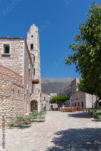 Greek village square with stone church bell tower and outdoor cafe