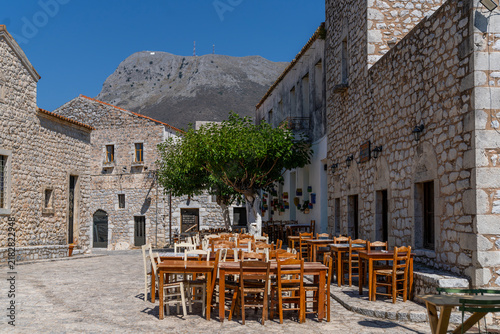Traditional Greek village square with outdoor cafe tables and mountain background