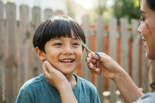 Mother gently cutting her young son's hair in the backyard, capturing a sweet family moment