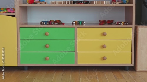 Colorful wooden furniture with green and yellow drawers in a kindergarten classroom. Shelves are filled with musical instruments for kids