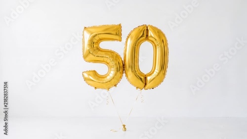 Gold number 50 foil balloons floating on a clean white background with copy space, festive decoration for 50th birthday, anniversary, milestone and jubilee celebration concepts.