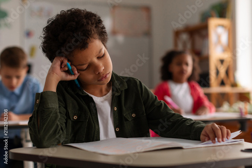 Foto Tired schoolboy writing in notebook in classroom, struggling with focus during l