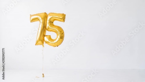 Gold number 75 foil balloons floating on a clean white background with copy space, festive decoration for 75th birthday, anniversary, jubilee and milestone celebration.