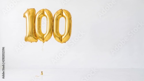 Gold number 100 foil balloons floating on a clean white background with copy space, festive decoration for 100th birthday, centenary, anniversary and milestone celebration.
