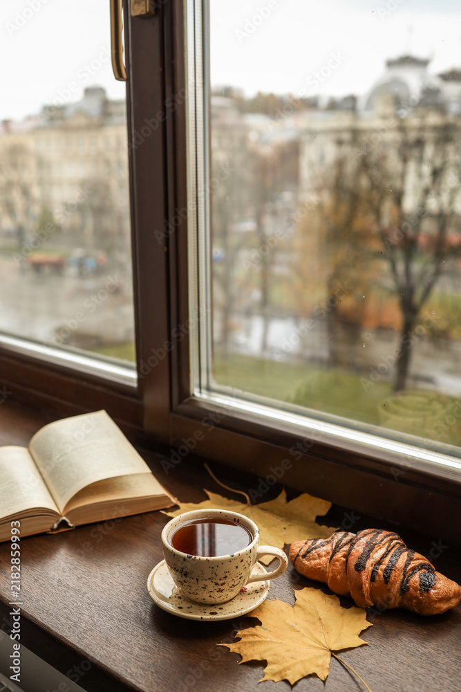 Obraz premium Cozy autumn morning with tea, croissant, and an open book by the window