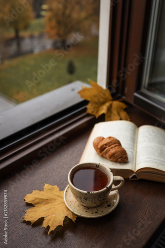 Cozy autumn morning with tea, croissant, and an open book by the window