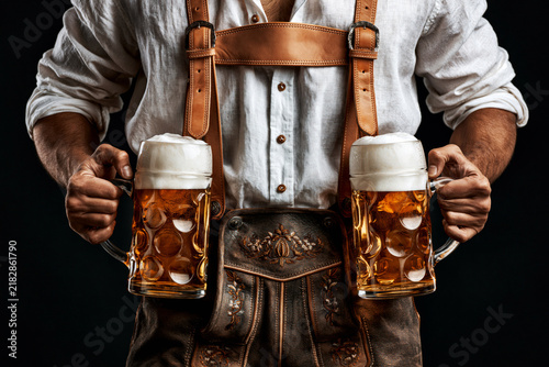 Man in Bavarian lederhosen holding two beer mugs isolated on black background with clipping path, Oktoberfest concept