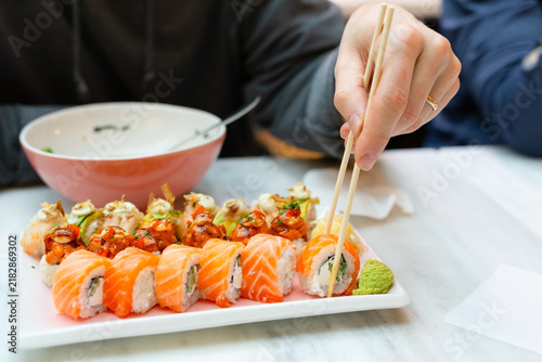 Man picking up sushi with chopsticks at a cozy Japanese restaurant. Diner enjoying authentic taste of fresh rolls during a satisfying meal. Businessman savoring traditional cuisine in inviting eatery