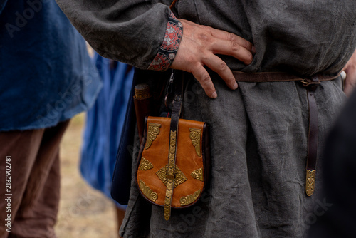 Medieval belt pouch made of brown leather with ornate brass plates worn on belt by reenactor in rustic linen tunic.