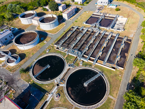 Overview of a wastewater treatment plant located in a suburban area showing large tanks and processing structures during the daytime