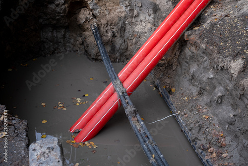 Red plastic pipes crossing over water inside underground sinkhole cavity, close up