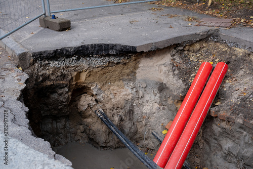 Sinkhole cross section showing soil layers and red pipes beside sidewalk, road collapse