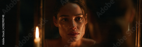 woman reflected in mirror by candlelight, mysterious woman looking into mirror illuminated by a single candle, intimate cinematic reflection of woman in warm candlelight and deep shadows