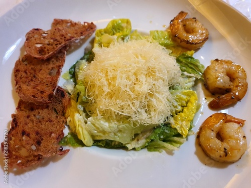 Bild auf Leinwand A Caesar salad served on a white plate, featuring fresh romaine lettuce leaves coated in creamy dressing, topped with a generous mound of shredded Parmesan cheese