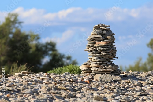 Foto Vue rapprochée d'un tas de galets plats empilés appelé cairn ou montjoie, construit sur une plage, avec de la végétation et un ciel bleu en arrière plan