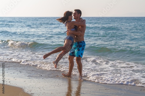 Happy cheerful young couple having fun water splashing, laughing and jumping at the beach with the ocean in the background.